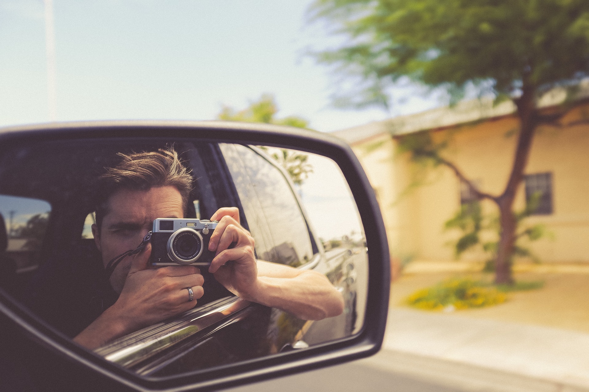 man taking photo reflected in wing mirror
